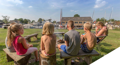 Kinderen zitten rond het kampvuur op jachthaven friesland en camping aan het water